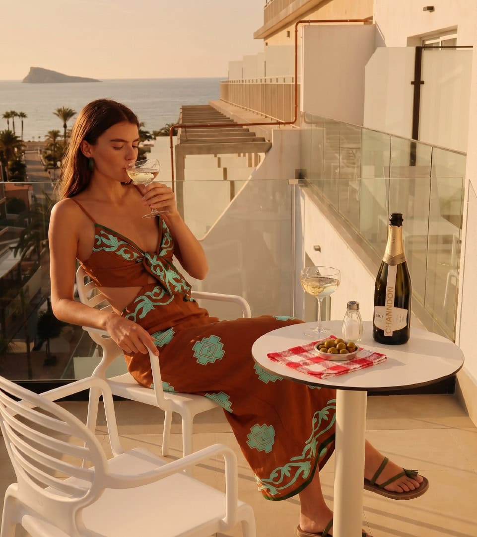 Mujer disfrutando de una copa de vino en terraza con vista al mar.