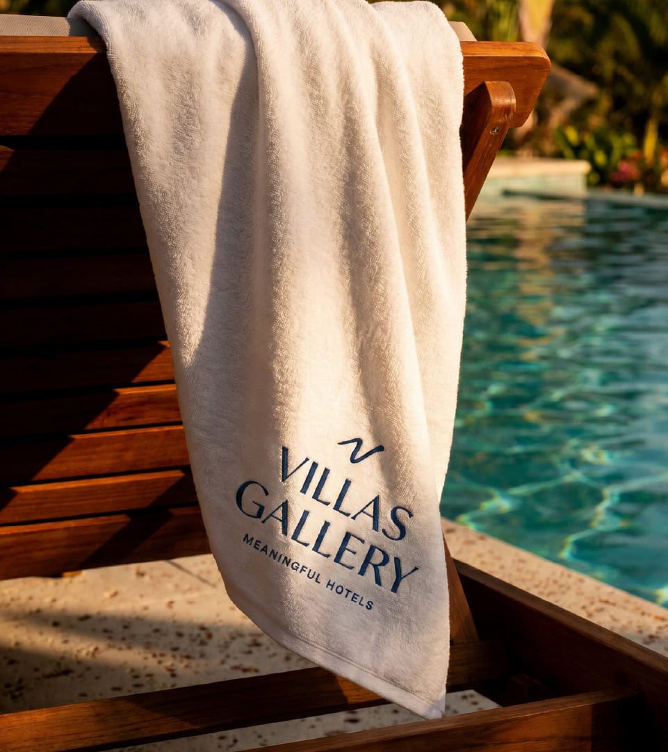 Toalla con logo Villas Gallery junto a piscina de hotel de lujo.