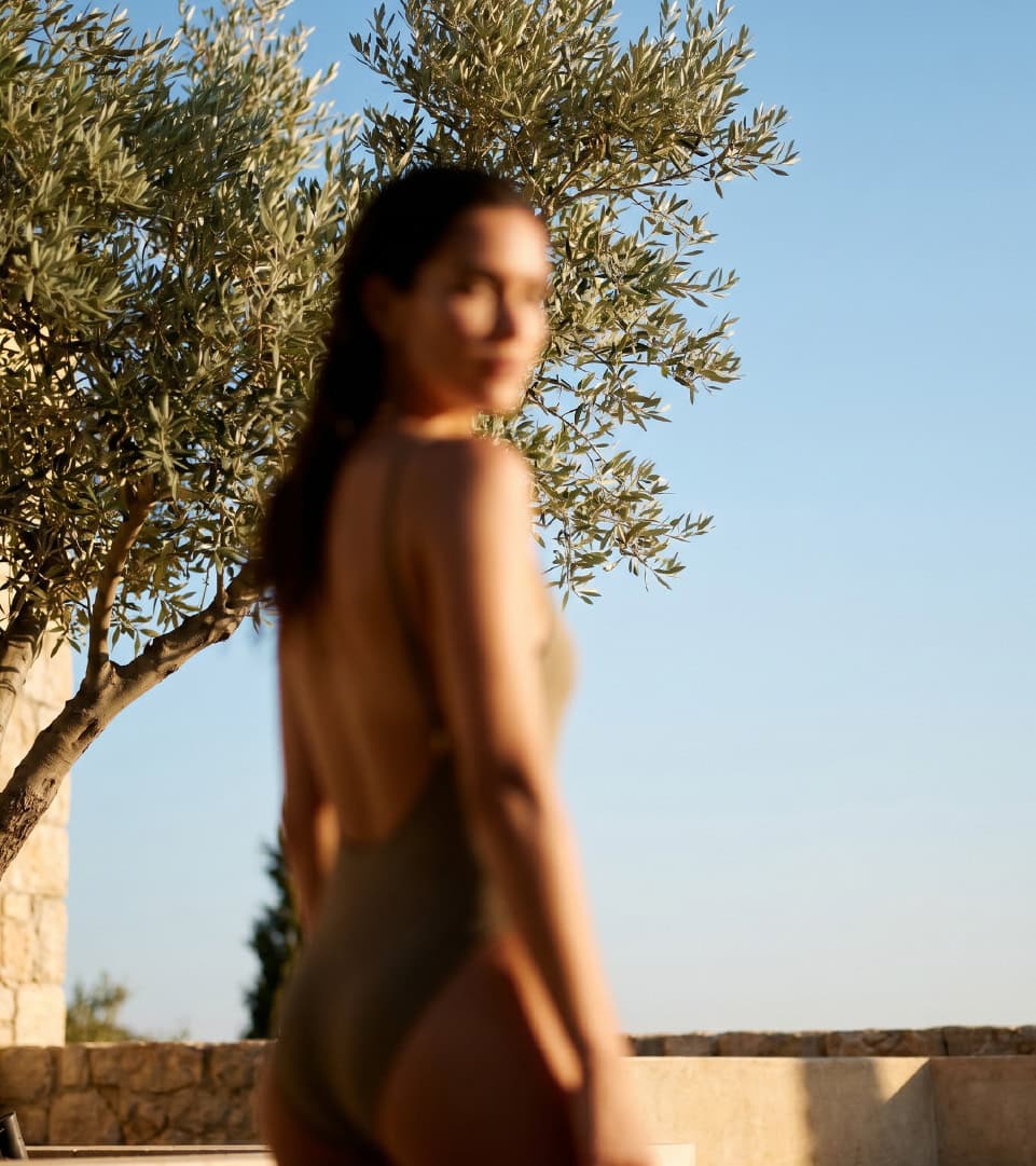 Mujer en traje de baño en un entorno al aire libre con árbol y cielo azul.